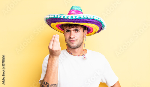 young handsome man making capice or money gesture, telling you to pay. mexican hat concept