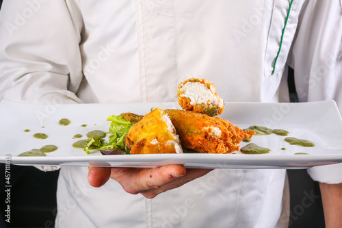 Piatto da ristorante tenuto in mano dallo chef con fiori di zucca fritti ripieni di ricotta fresca e accompagnati da una salsa al basilico  photo