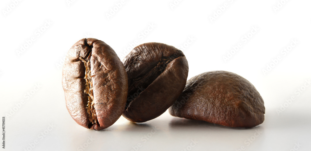 Fototapeta premium Macro of three coffee beans on white table front