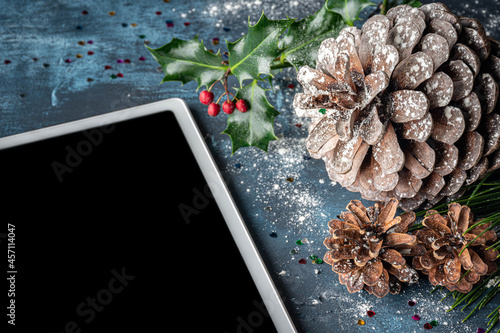 Tableta digital con decoración navideña: piña de pino, acebo y piñas de conífera. Vista lateral. photo