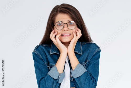Closeup portrait nervous stressed young woman girl in glasses student biting fingernails looking anxiously craving something isolated on white wall background. Human emotion face expression feeling