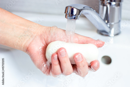 Young caucasian woman washes hands with water and soap in the bathroom.