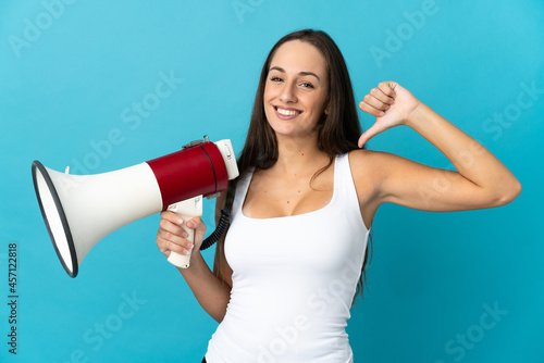 Young hispanic woman over isolated blue background holding a megaphone and proud and self-satisfied