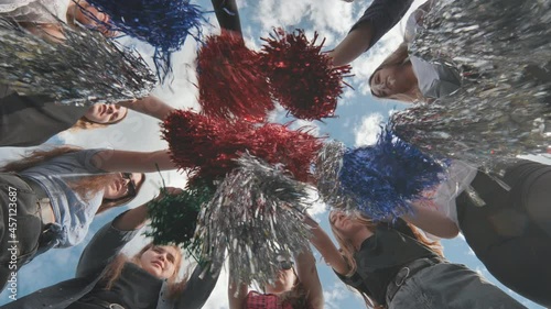 Cheerful girls in the meadow waving multi-colored cheerleading pompoms. photo