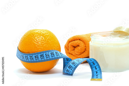 Fruit orange is wrapped with blue measuring tape, body scrub and towel on white background. Orange peel as symbol of cellulite on skin. Anti-cellulite creative concept.