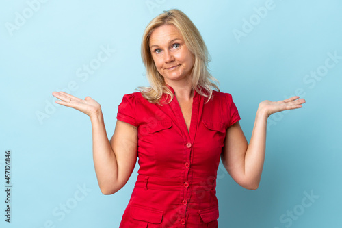 Middle age woman isolated on blue background having doubts while raising hands © luismolinero