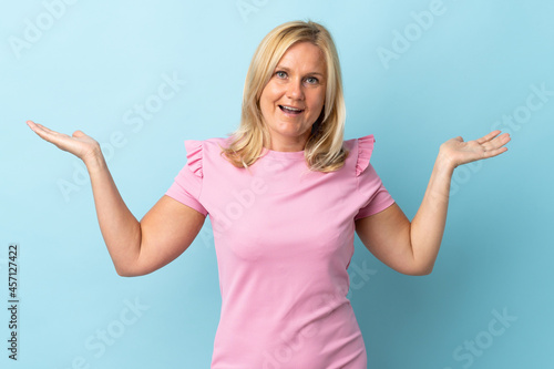 Middle age woman isolated on blue background with shocked facial expression