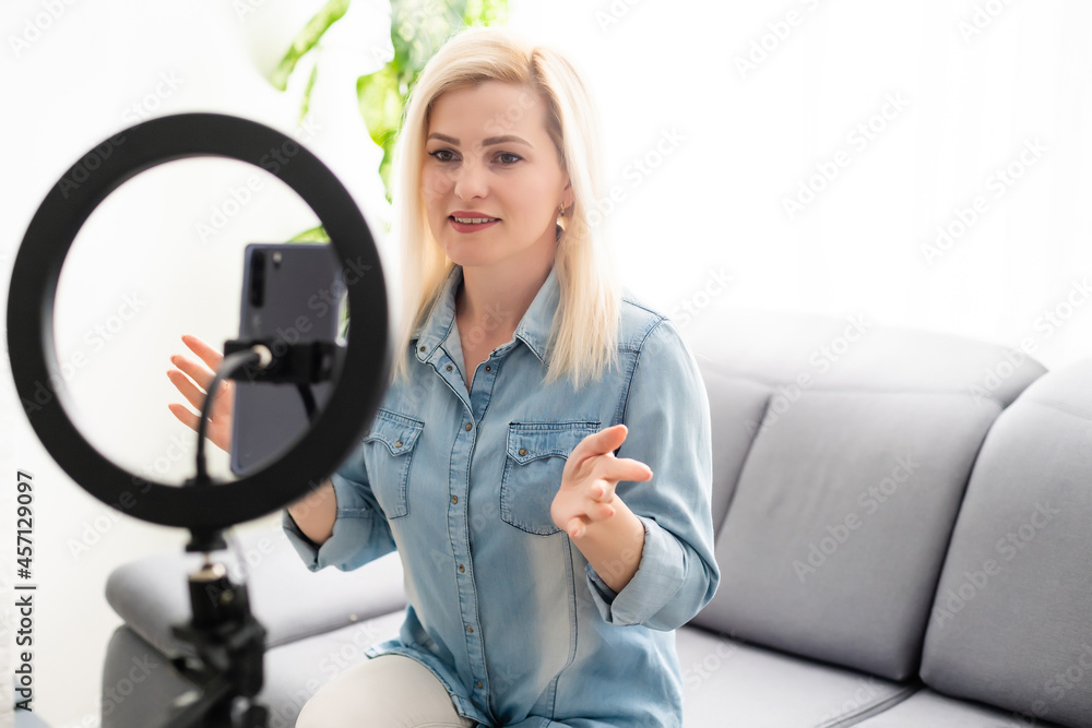A young woman works, conducts live broadcasts from home by the Internet. female talks, leads a lesson, blog online. female blogger writes a blog issue using round lamp A young woman works, conducts live broadcasts from home by the Internet. female talks, leads a lesson, blog online. female blogger writes a blog issue using round lamp