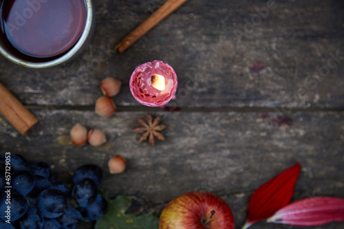 Rustic natural cozy still life:candle, fruits, hazelnuts, anise star and cup of tea. Autumn aesthetic concept, red georgine petals. Cozy home with aromatic candle. Thanksgiving Day concept. Copy space