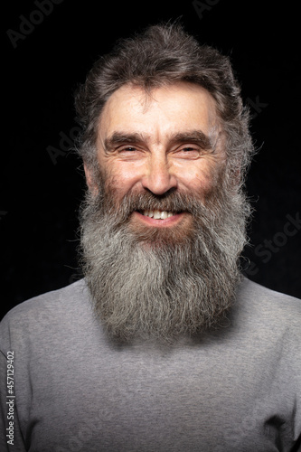 The face of an elderly smiling man with a gray beard on a black background.