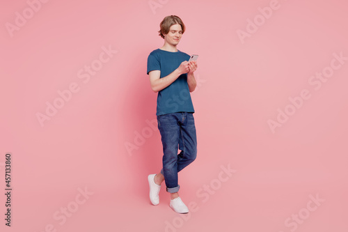 Full length photo of young guy happy positive smile chat type sms cellphone isolated over pink color background