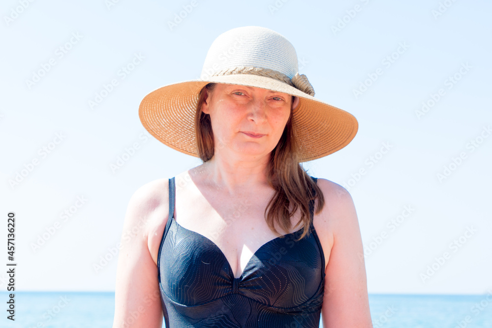 Summer portrait of a beautiful woman 40 years old in a straw hat at the sea.