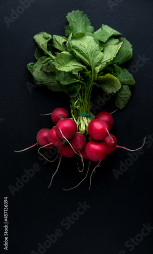A bunch of radishes on a black background. Low key, natural light, selective focus. Top view, flat lay, copy space