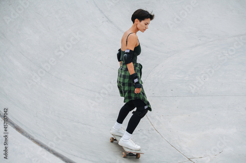 Immersed woman skater with short hair riding on her board on quarter pipe circle