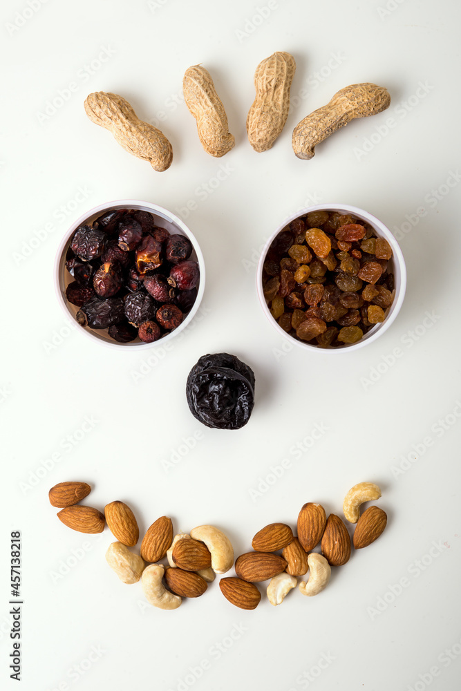 Set of raisins, rose hips, peanuts, almonds, cashews and prunes fomed in cute face shape. top view on white background Set of raisins, rose hips, peanuts, almonds, cashews and prunes fomed in cute face shape. top view on white background