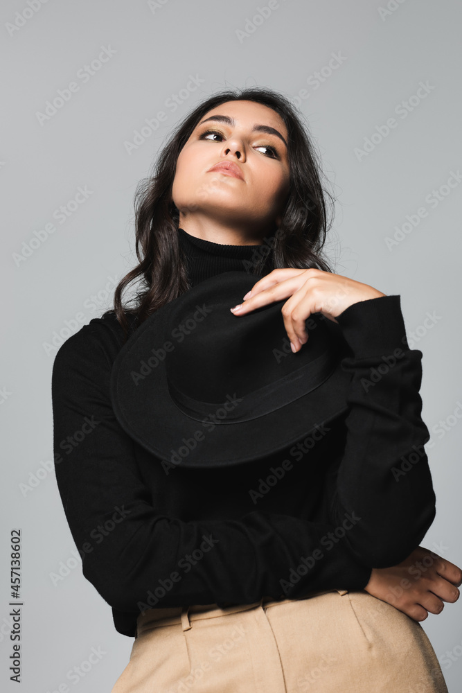 young model holding black fedora hat and looking away isolated on grey young model holding black fedora hat and looking away isolated on grey