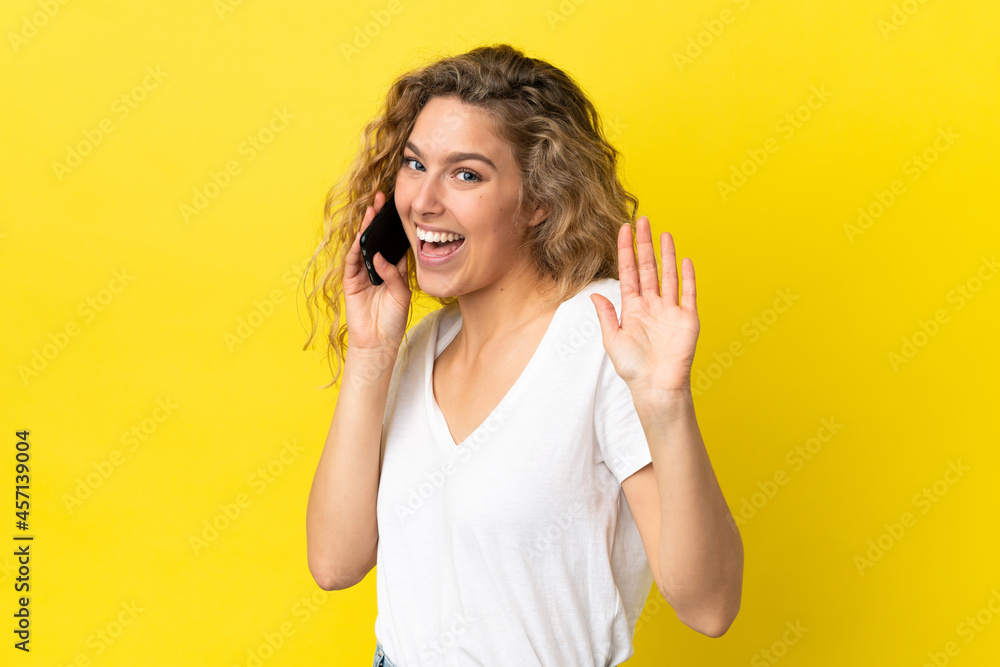 Young blonde woman using mobile phone isolated on yellow background saluting with hand with happy expression Young blonde woman using mobile phone isolated on yellow background saluting with hand with happy expression