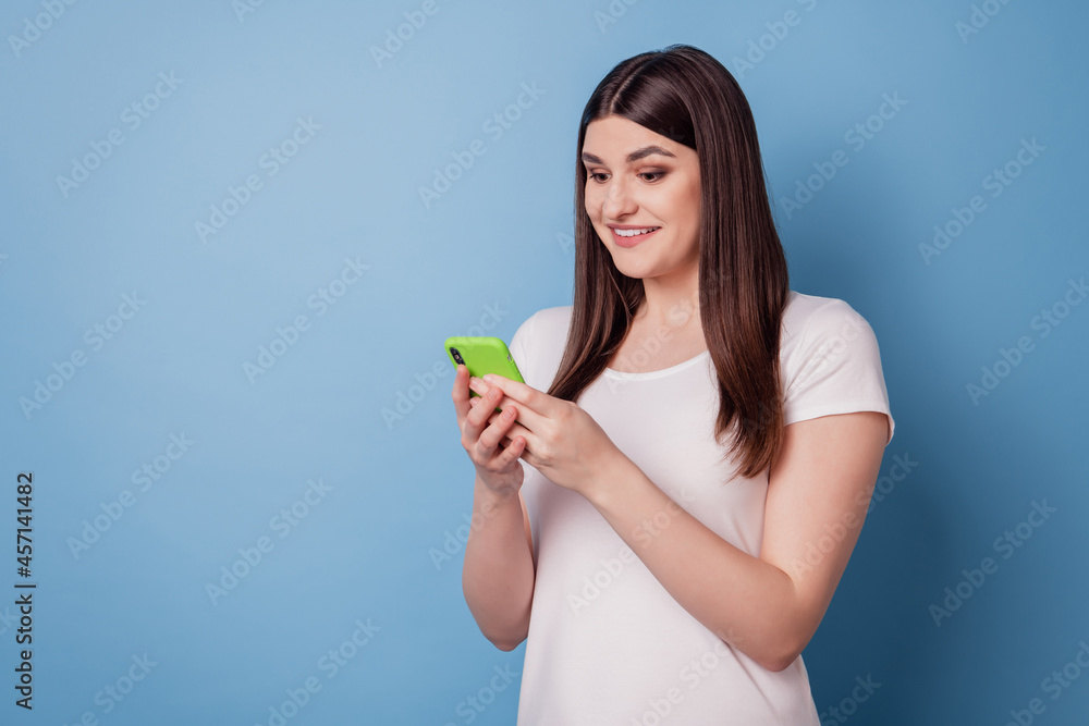 Portrait of charming excited pretty lady hold cellphone look screen toothy smile on blue background Portrait of charming excited pretty lady hold cellphone look screen toothy smile on blue background