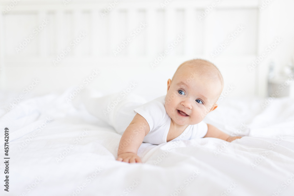 Portrait of cute and smiling four month old baby girl playing on the bed in her room. Happy and dry kid. 