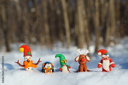 Snowman, Santa, deer, dwarf, and penguin figurines in a snowy forest. Fabulous new year characters.