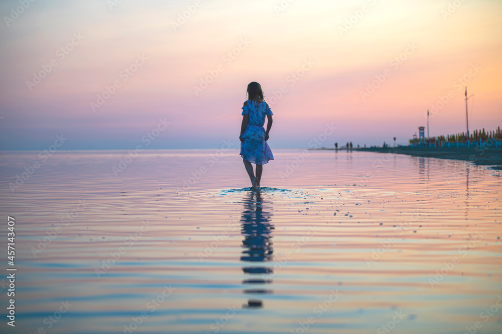 a girl in a dress on the seashore at sunset walks on the water