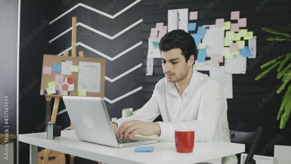 A thoughtful young man of Caucasian appearance is sitting at a computer and working remotely. The young man works remotely A thoughtful young man of Caucasian appearance is sitting at a computer and working remotely. The young man works remotely