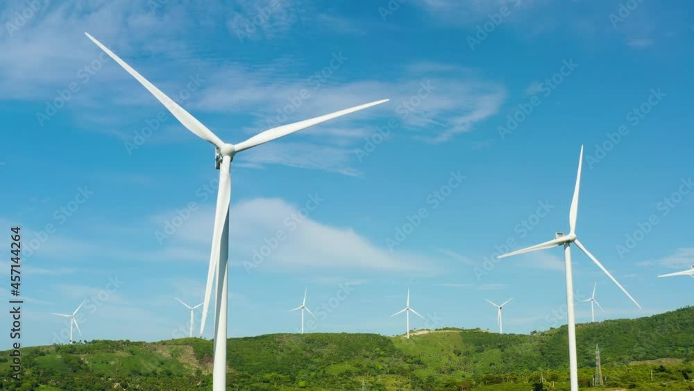 Beautiful white wind turbines are spinning large blades in a green field.