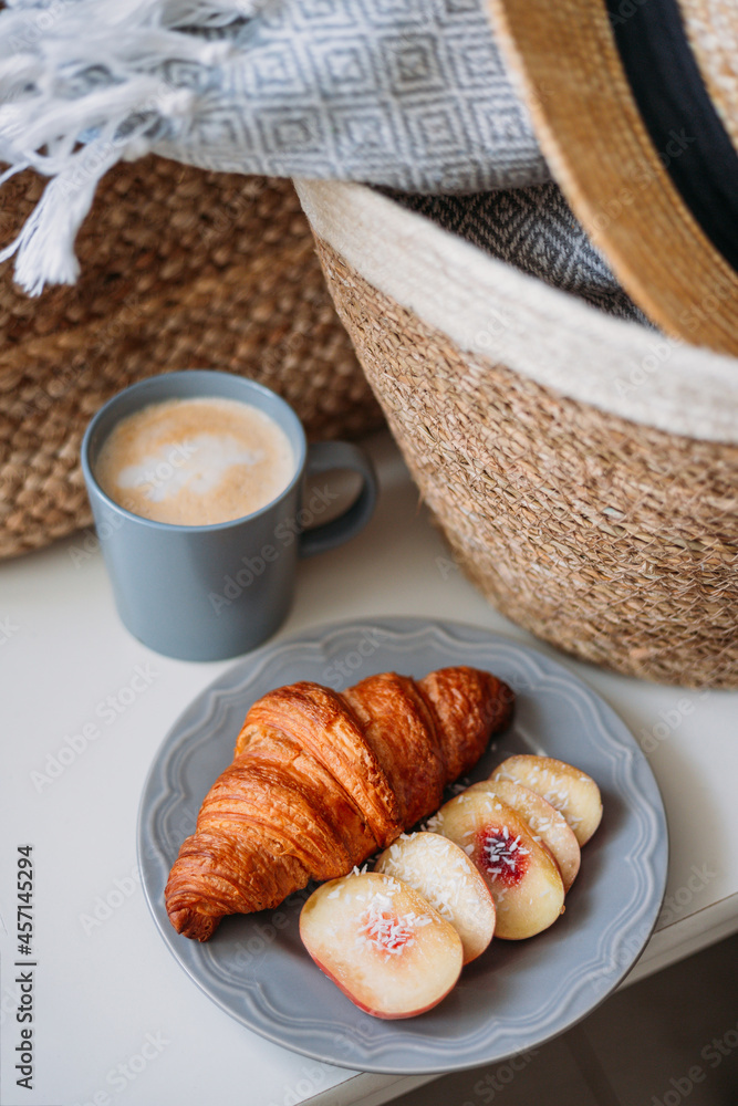 Freshly baked croissant and coffee mug. Coffee in cup on wooden table in cafe. Basket with a gray plaid and a hat, top view