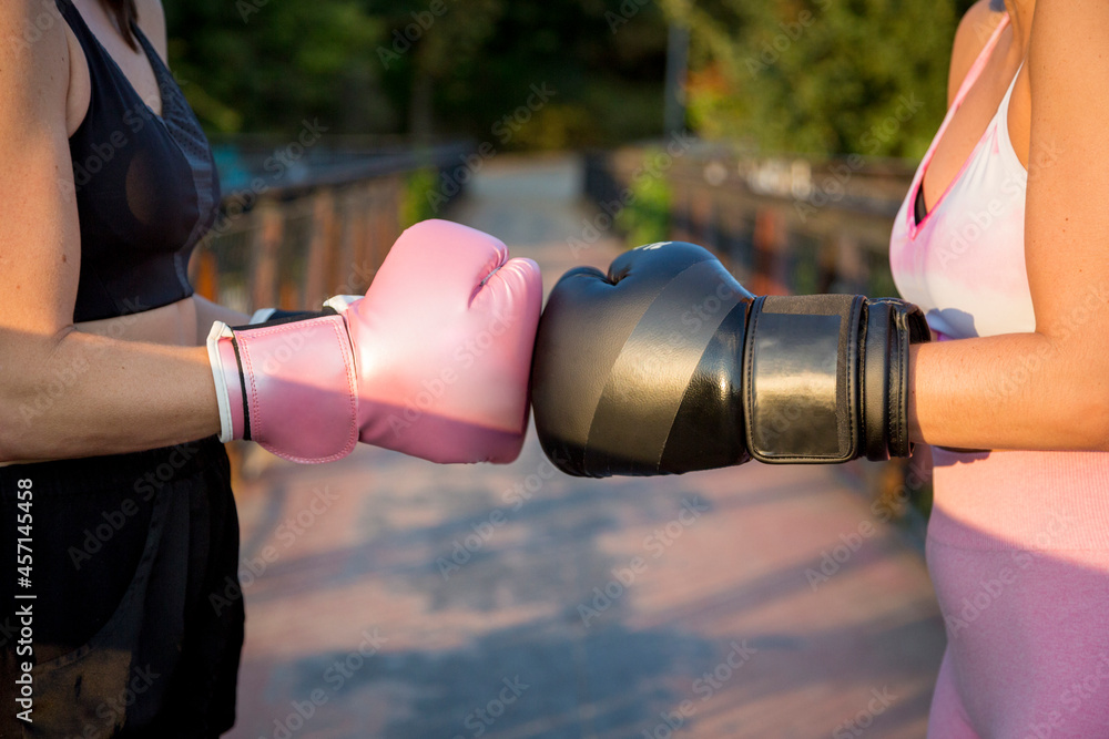 © luisrojasstock - Young caucasian women crashing boxing gloves on a bridge at sunset