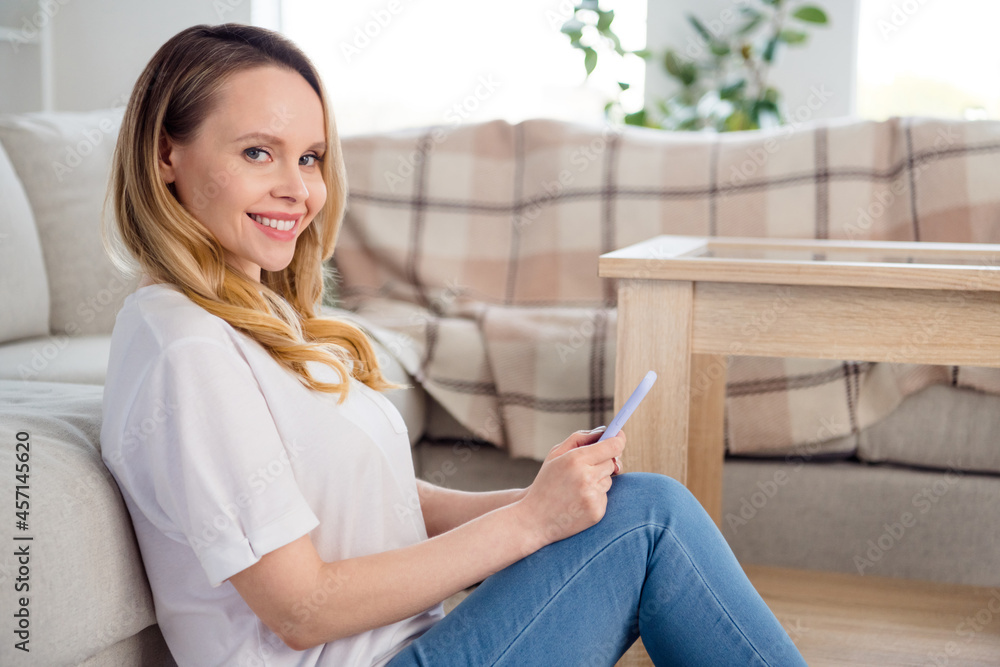 Profile side photo of young cheerful woman happy positive smile sit floor comfort use cellphone self-isolation indoors Profile side photo of young cheerful woman happy positive smile sit floor comfort use cellphone self-isolation indoors