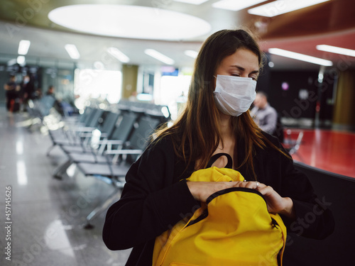 tired woman wearing medical mask eyes closed airport yellow backpack