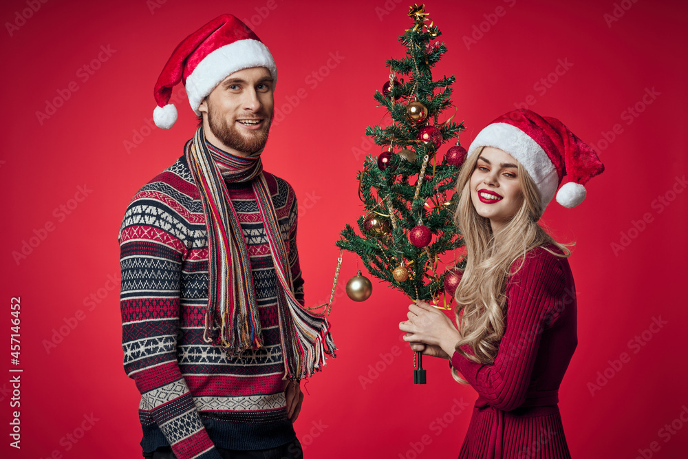 man and woman standing next to christmas tree toys lifestyle red background man and woman standing next to christmas tree toys lifestyle red background