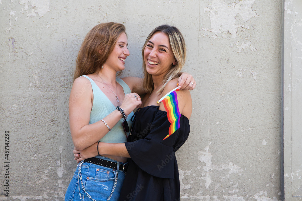 Beautiful young women are hugging each other with a gay pride flag in their hand. The girls are lesbians and are demanding equality between people of the same sex. Concept of equality and diversity.