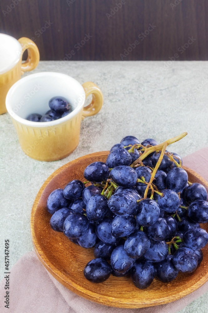 In a wooden plate there is a vine with ripe dark-colored fruits and a stone inside In a wooden plate there is a vine with ripe dark-colored fruits and a stone inside