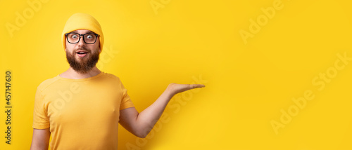 handsome caucasian man showing empty open hand over yellow background, panoramic layout with space for text