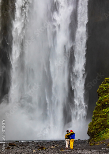 couple facing the powerful Skogafoss waterfall in Iceland.