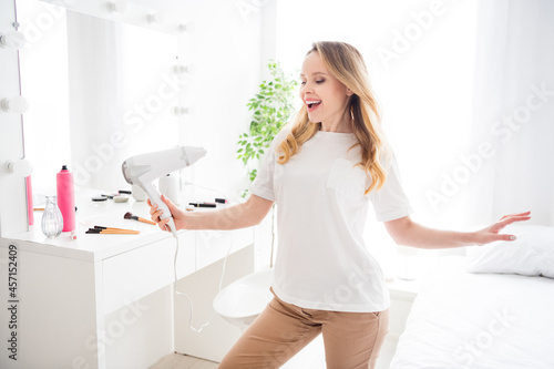 Photo portrait young woman in white outfit blonde drying hair with dryer smiling happy in the morning