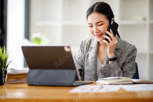 Portrait of Asian young Businesswoman talking on cell phone working on table computer in office hallway,blur background.