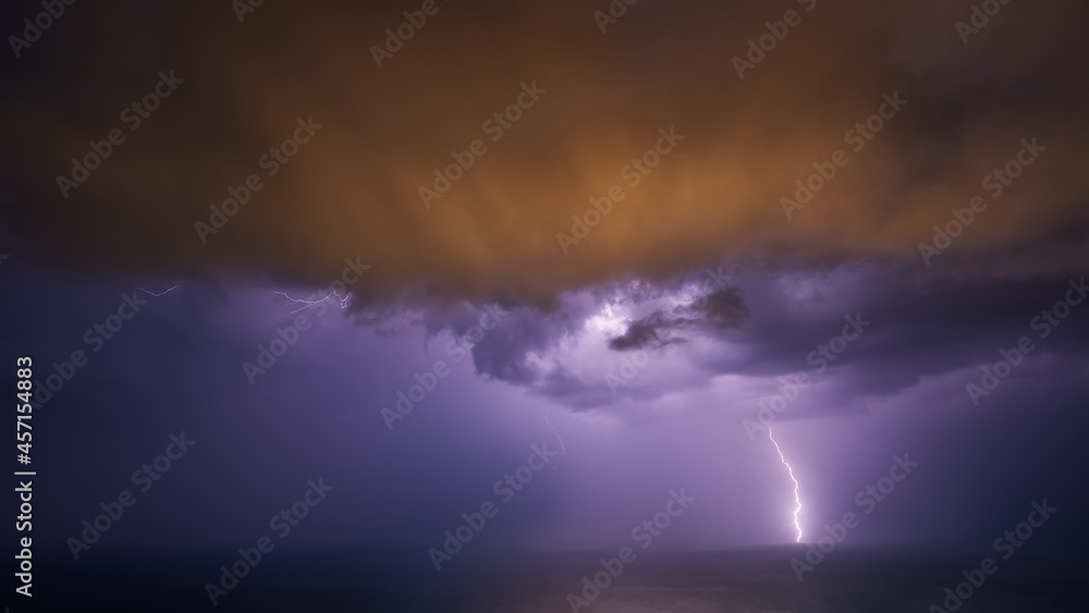 A night thunderstorm over the sea with multicolored clouds.