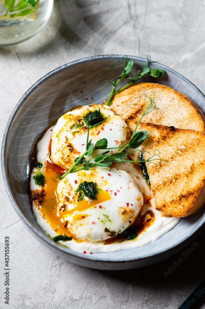 Cilbir or Turkish Eggs. dish served as mezze: poached eggs topped over herbed greek yogurt, then drizzled with hot spiced paprika olive oil. Turkish breakfast in a grey bowl on marble background Cilbir or Turkish Eggs. dish served as mezze: poached eggs topped over herbed greek yogurt, then drizzled with hot spiced paprika olive oil. Turkish breakfast in a grey bowl on marble background