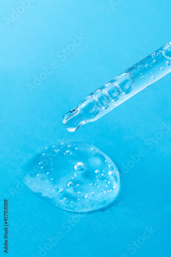Transparent facial serum with bubbles in glass pipette on light blue background closeup. Liquid gel drop for skin care macro. Beauty concept. Cosmetic product advertising.  © gorina_anna