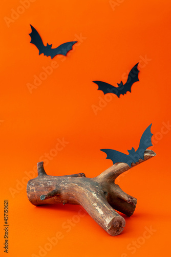 Empty wooden podium and black paper bats on bright orange background. Halloween still life photo. Mockup for cosmetic product. Piece of wood for cosmetic presentation. Front view.