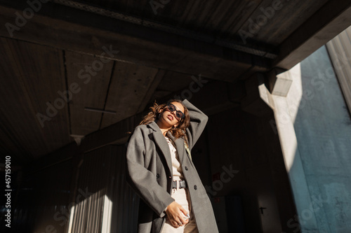 Fashion beautiful curly-haired girl with vintage sunglasses in stylish casual clothes look on an urban background `in sunlight