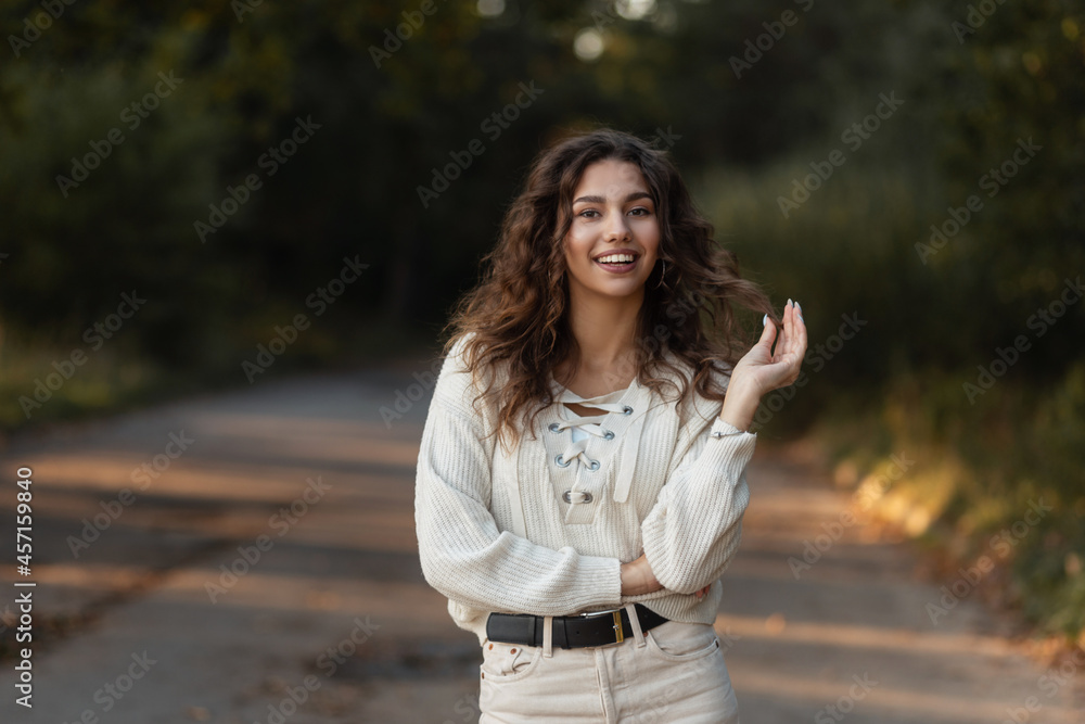 Beautiful fresh portrait of a young happy woman with curly hair and a pretty smile in a stylish knitted blouse on nature in the park Beautiful fresh portrait of a young happy woman with curly hair and a pretty smile in a stylish knitted blouse on nature in the park