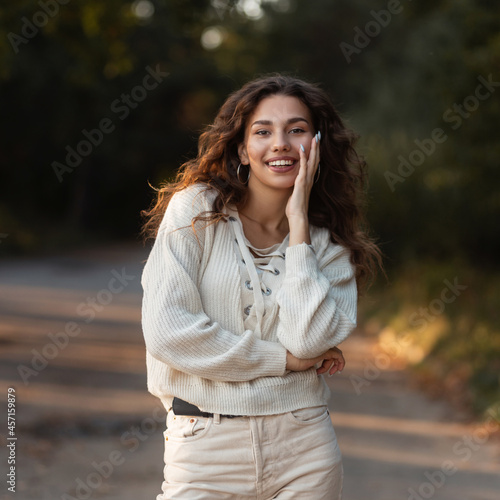 Lovely young happy girl with a cute smile in a knitted sweater relaxes an outdoors in the park. Pretty smiling female face