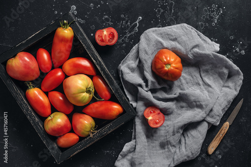 Fresh red tomatoes on a black stone background. Autumn harvest concept. Top view, flat lay.
