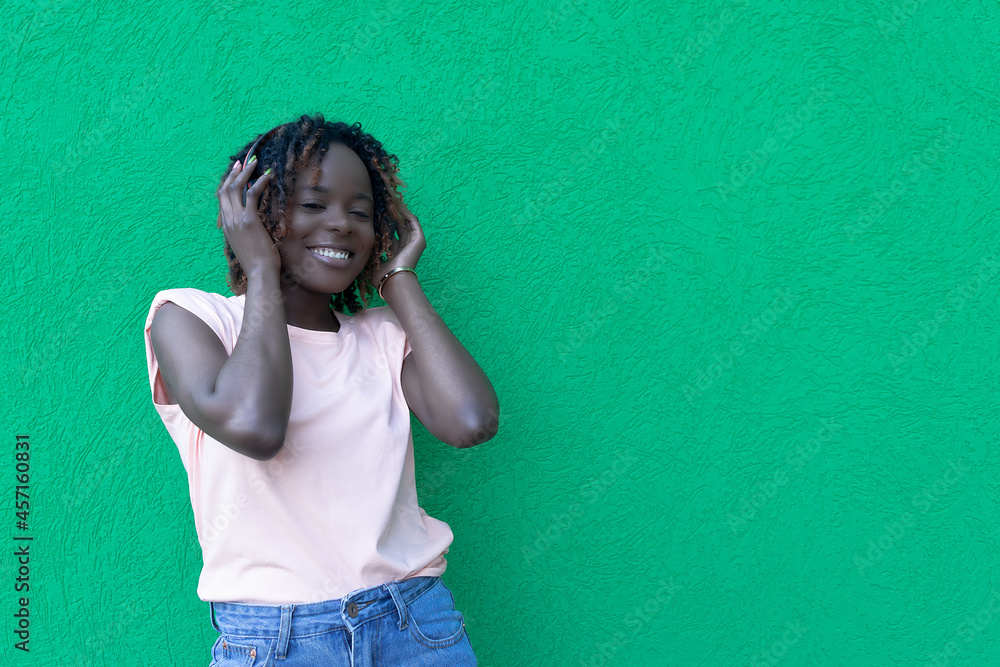The concept of lifestyle and people - a smiling African-American young woman listening to music with headphones. The joy and emotions of a person The concept of lifestyle and people - a smiling African-American young woman listening to music with headphones. The joy and emotions of a person