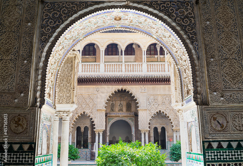 Beautiful arabian style decorated arch in the famous Alcazar (meaning: fortress) in Seville, Andalusia, Spain. A patio with green plants in the middle.
