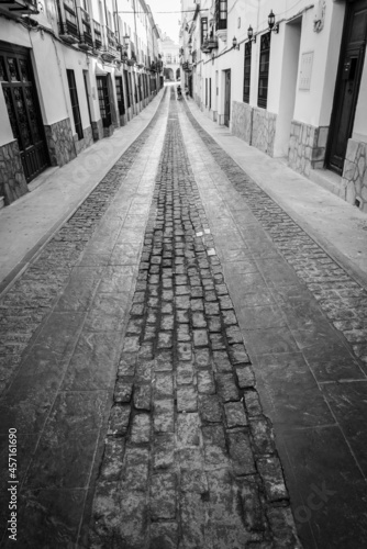 Narrow pedestrian alley with sidewalks and cobblestone ground in the historical centre of Ronda, Andalusia, Spain. Monochromatic.