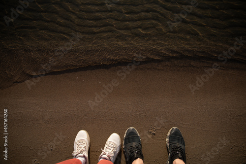 female legs in white sneakers and male legs in black sneakers on the seashore